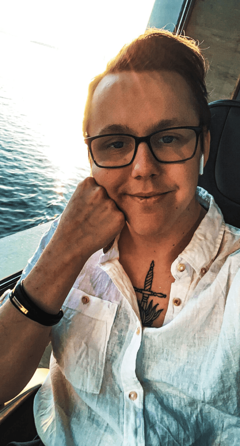 Portrett av Madsen med briller og hvit skjorte ved et vindu mot sjøen.