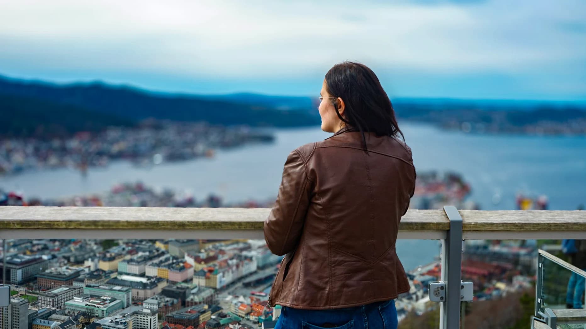 Person i brun jakke som ser ut over byen og fjorden fra et utsiktspunkt.
