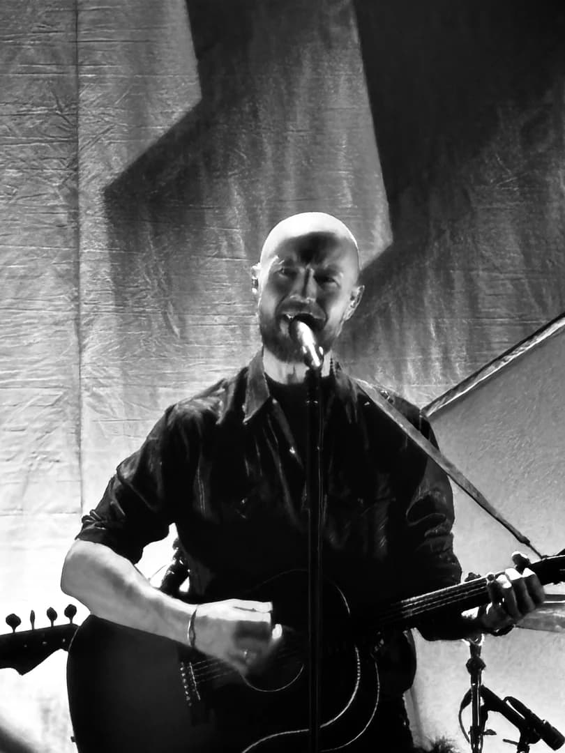 Sort-hvitt-fotografi av en gitarist som synger på scenen.